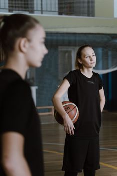 Young women basketball players in sportswear on an indoor court holding a basketball.