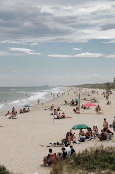 Crowded beach scene showcasing tourists relaxing under umbrellas with cloudy sky above.