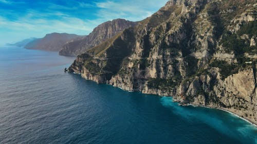 An Aerial Photography of a Mountain Near the Body of Water Under the Blue Sky and white Clouds