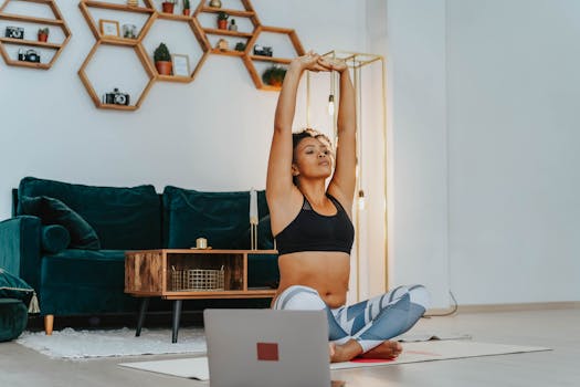 A woman in sportswear practicing yoga at home with a laptop nearby.