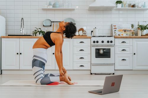 Free Fit woman doing yoga with laptop guidance in a stylish kitchen. Stock Photo