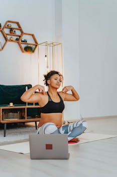 African American woman practicing yoga at home with a laptop, focusing on fitness and relaxation.