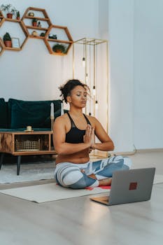 Calm woman doing yoga and meditation at home using an online class on her laptop.
