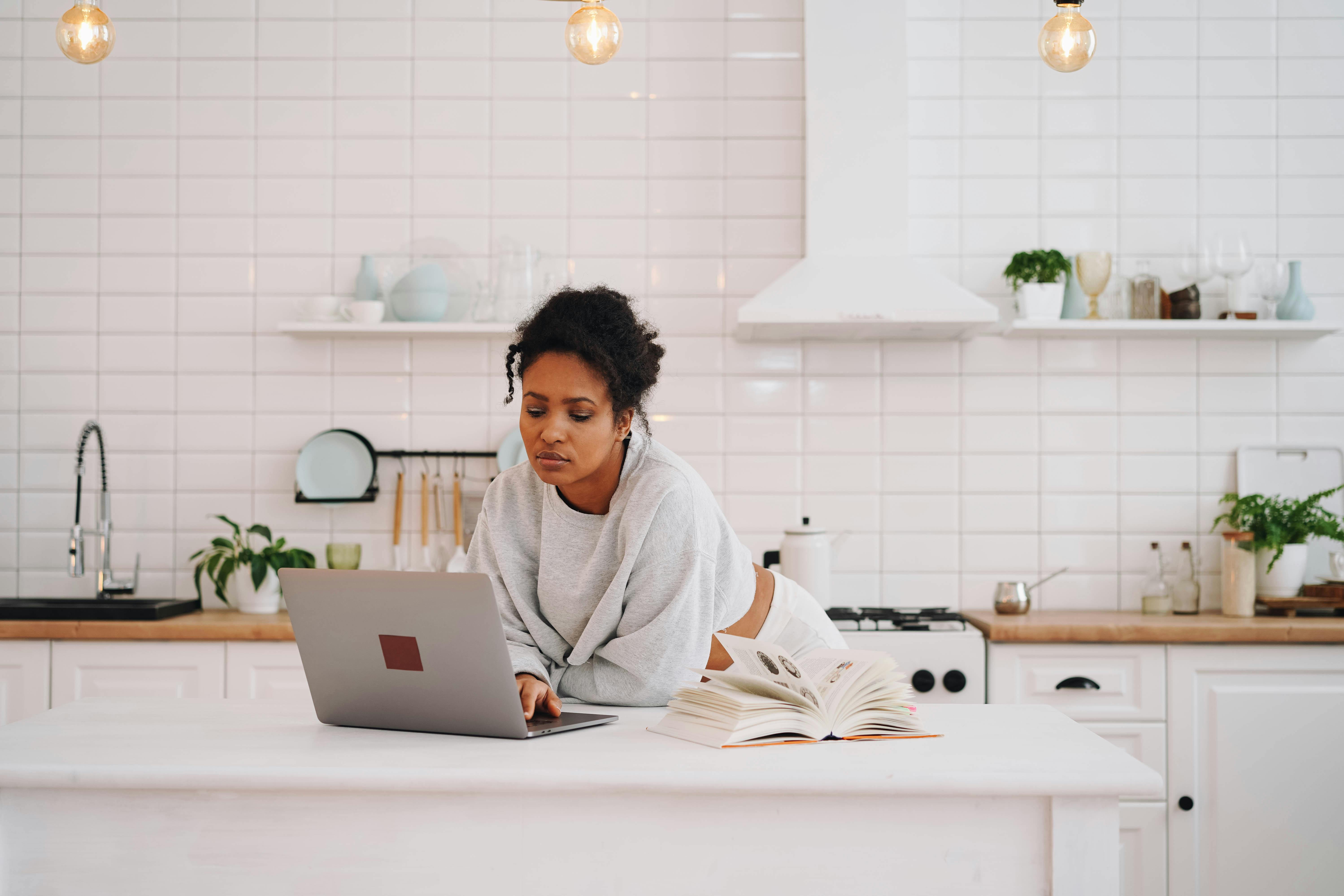 Young woman using laptop for distance learning in a stylish kitchen.