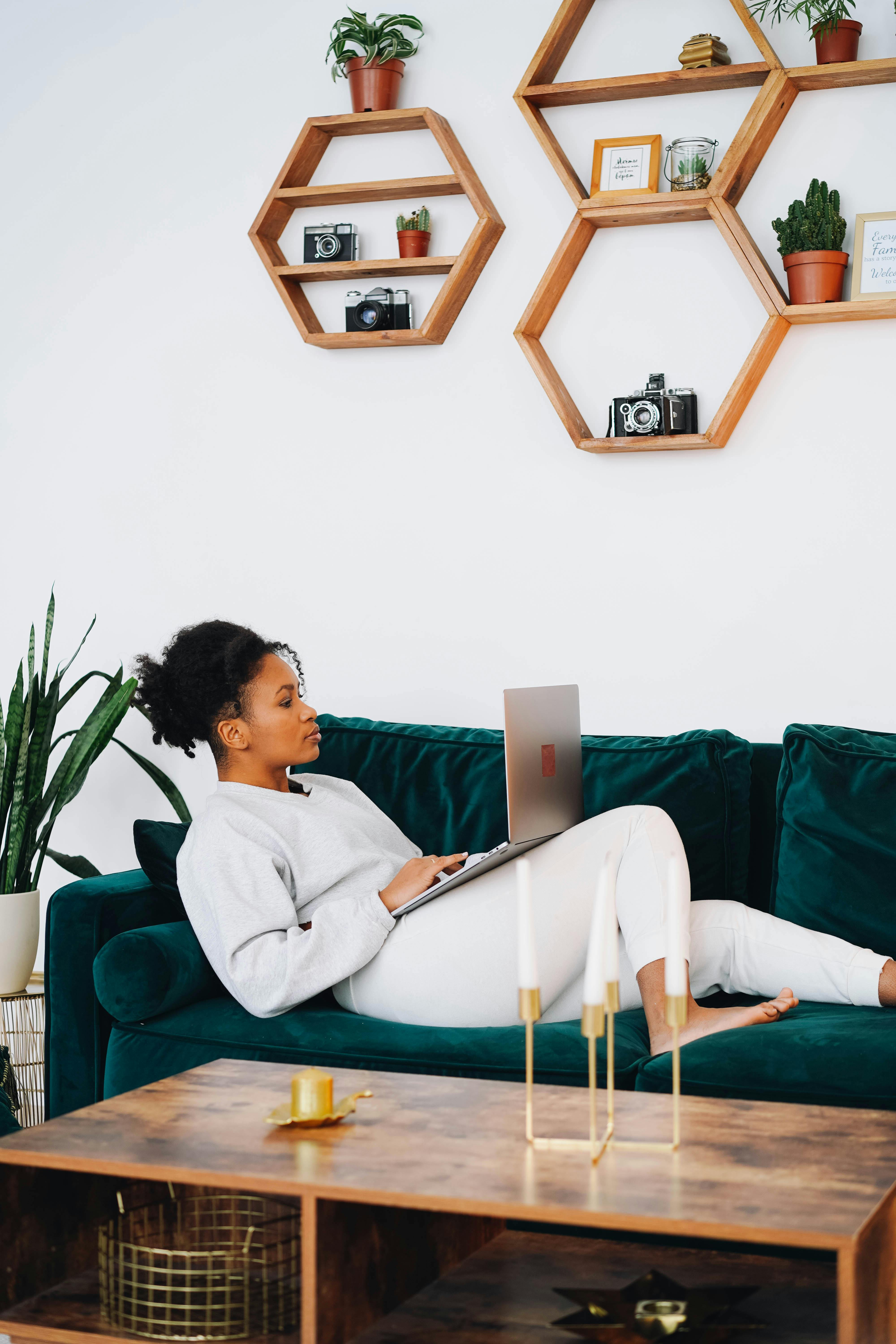 a woman sweater and pants lying on the couch while using her laptop