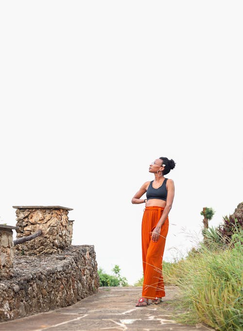 A Woman in a Pose Wearing Black Top and Orange Pants 
