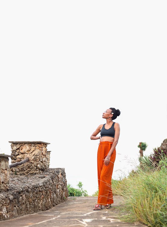 A Woman in a Pose Wearing Black Top and Orange Pants 