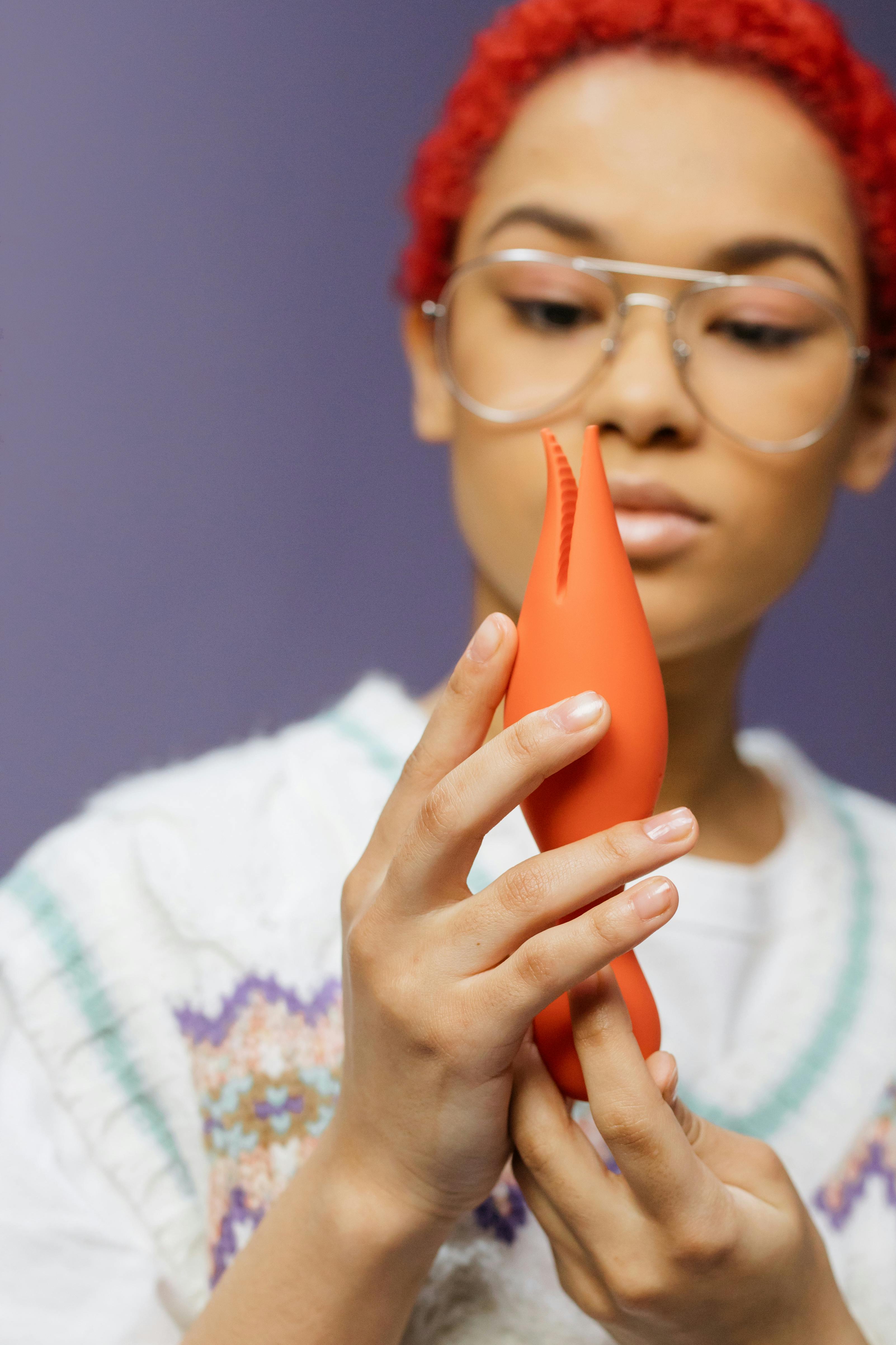 a woman wearing eyeglasses holding orange sex toy