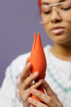 A woman holding a bright orange toy, focusing on sensuality and modern design.