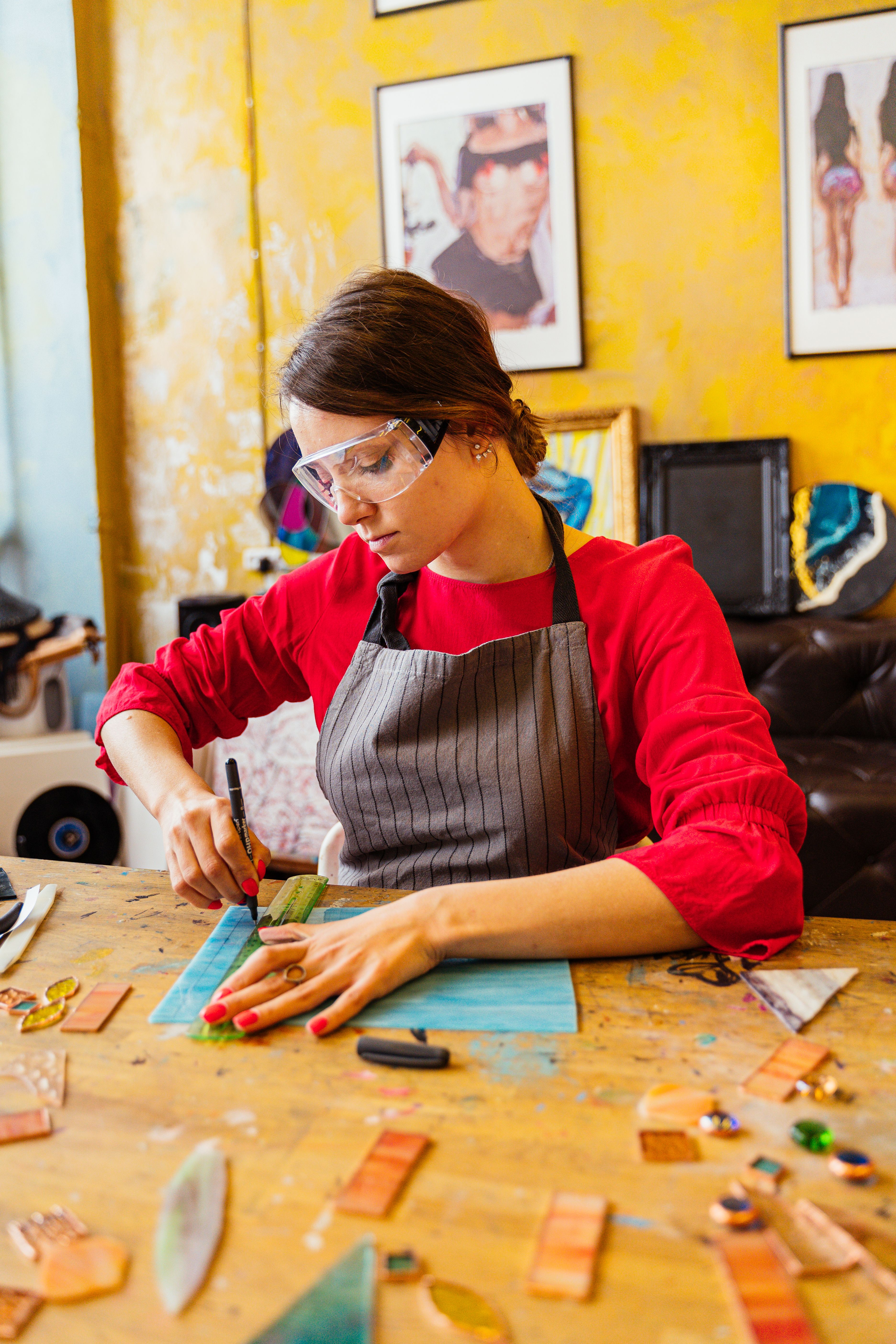 Woman in apron and goggles creating stained glass art in a vibrant studio.