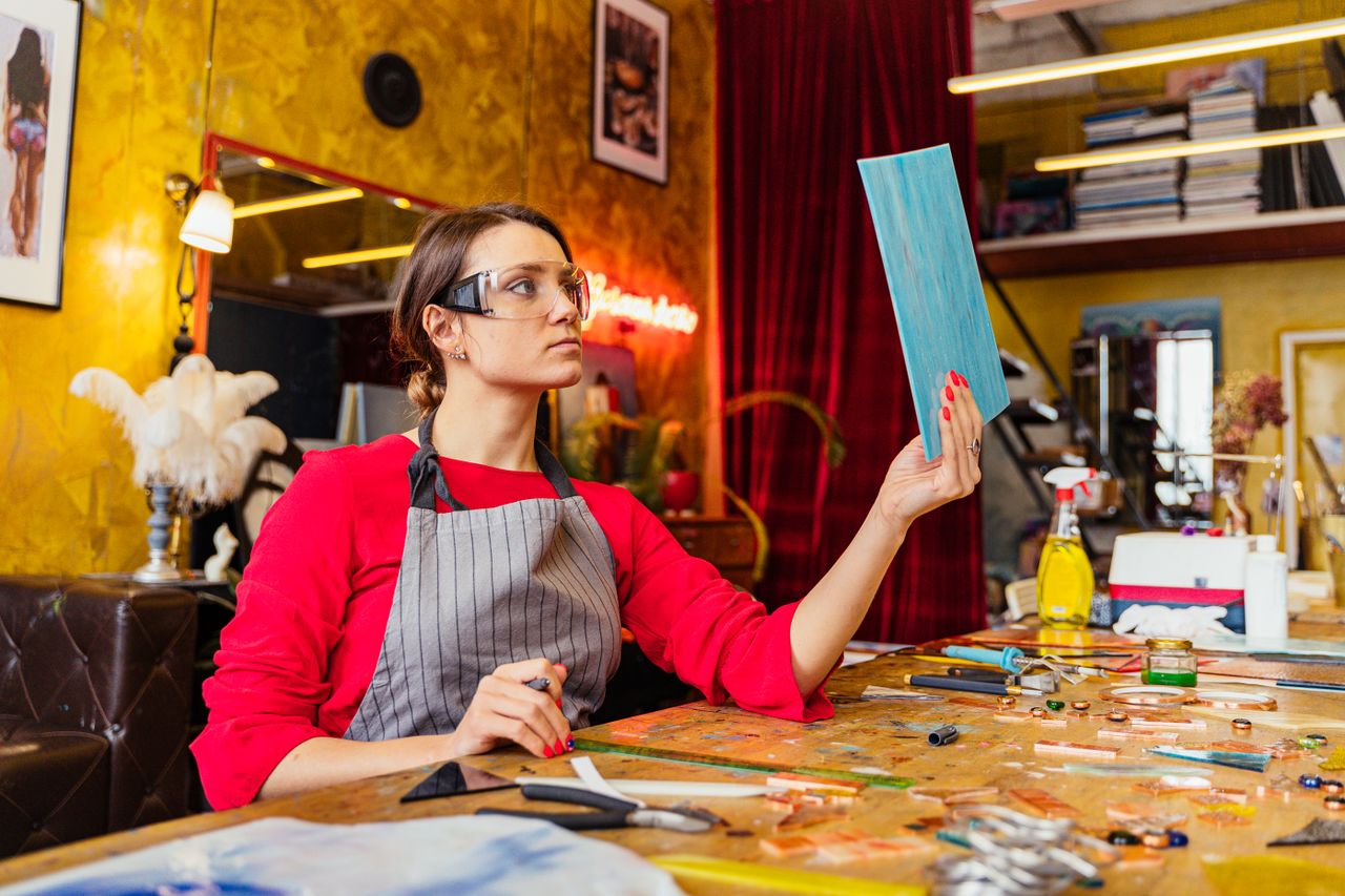 a woman artist in a vibrant studio holding a painted board surrounded
