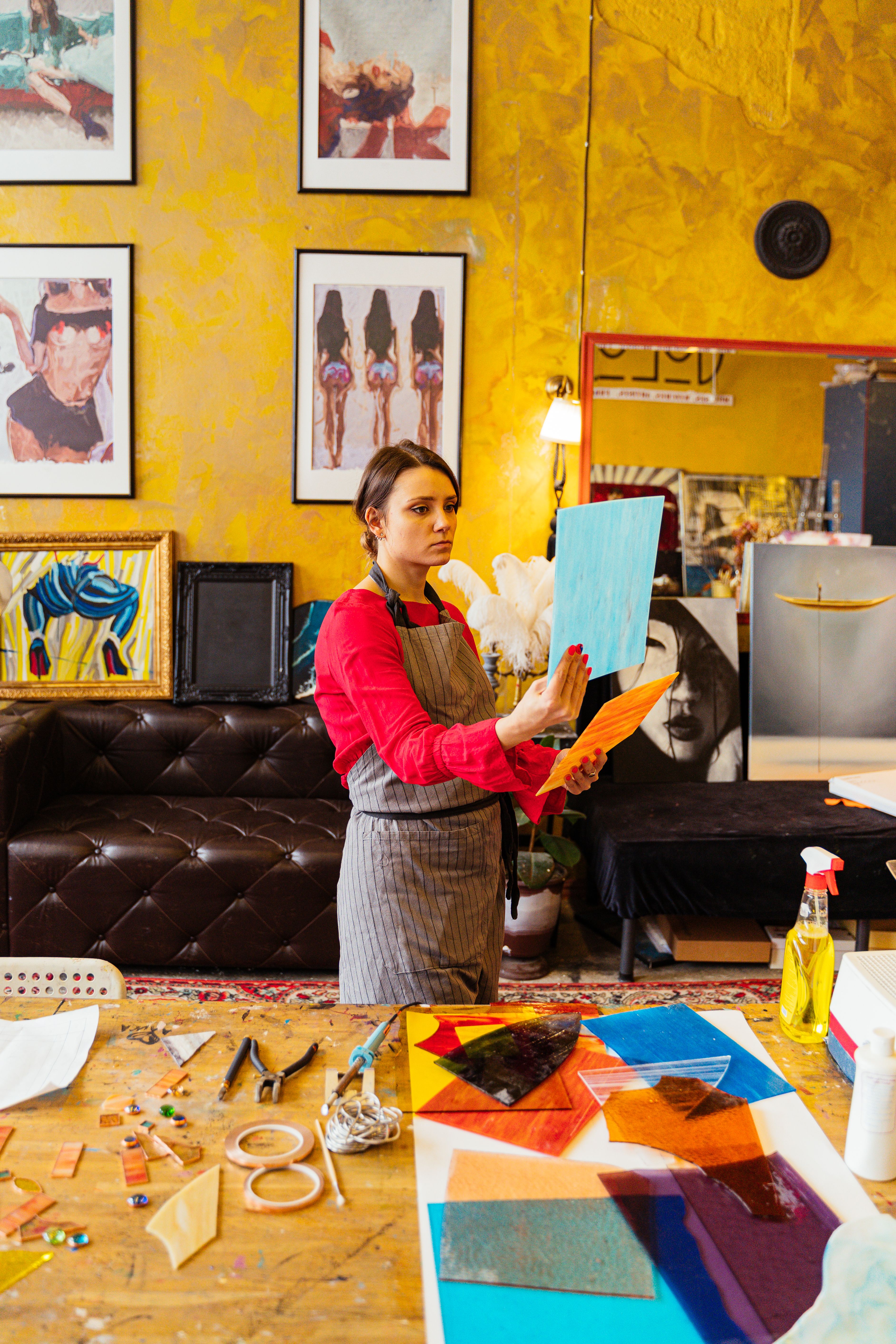 Woman engaged in stained glass art in a vibrant workshop setting with artistic decor.