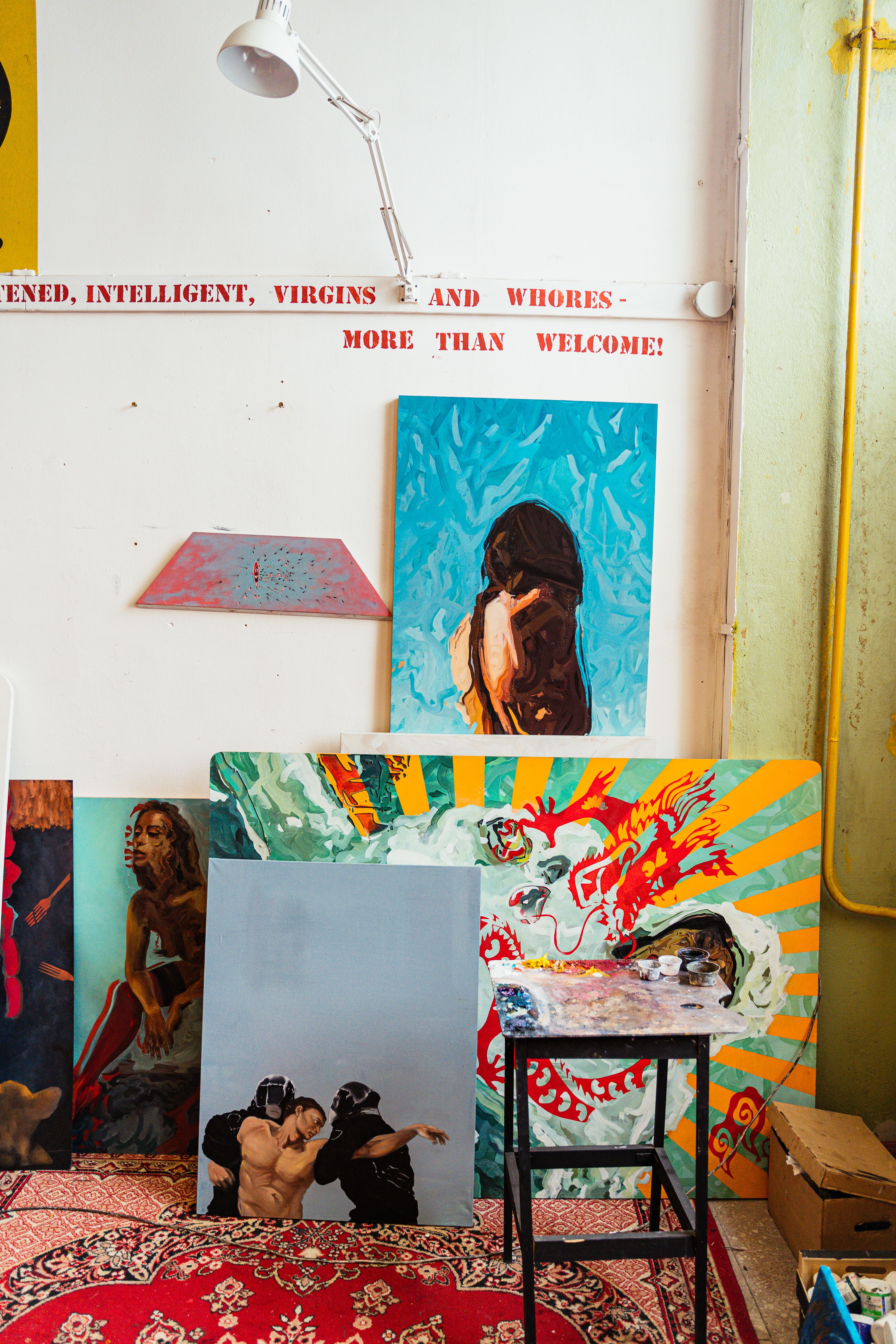 A lively art studio showcasing vibrant paintings and a stool for artists.