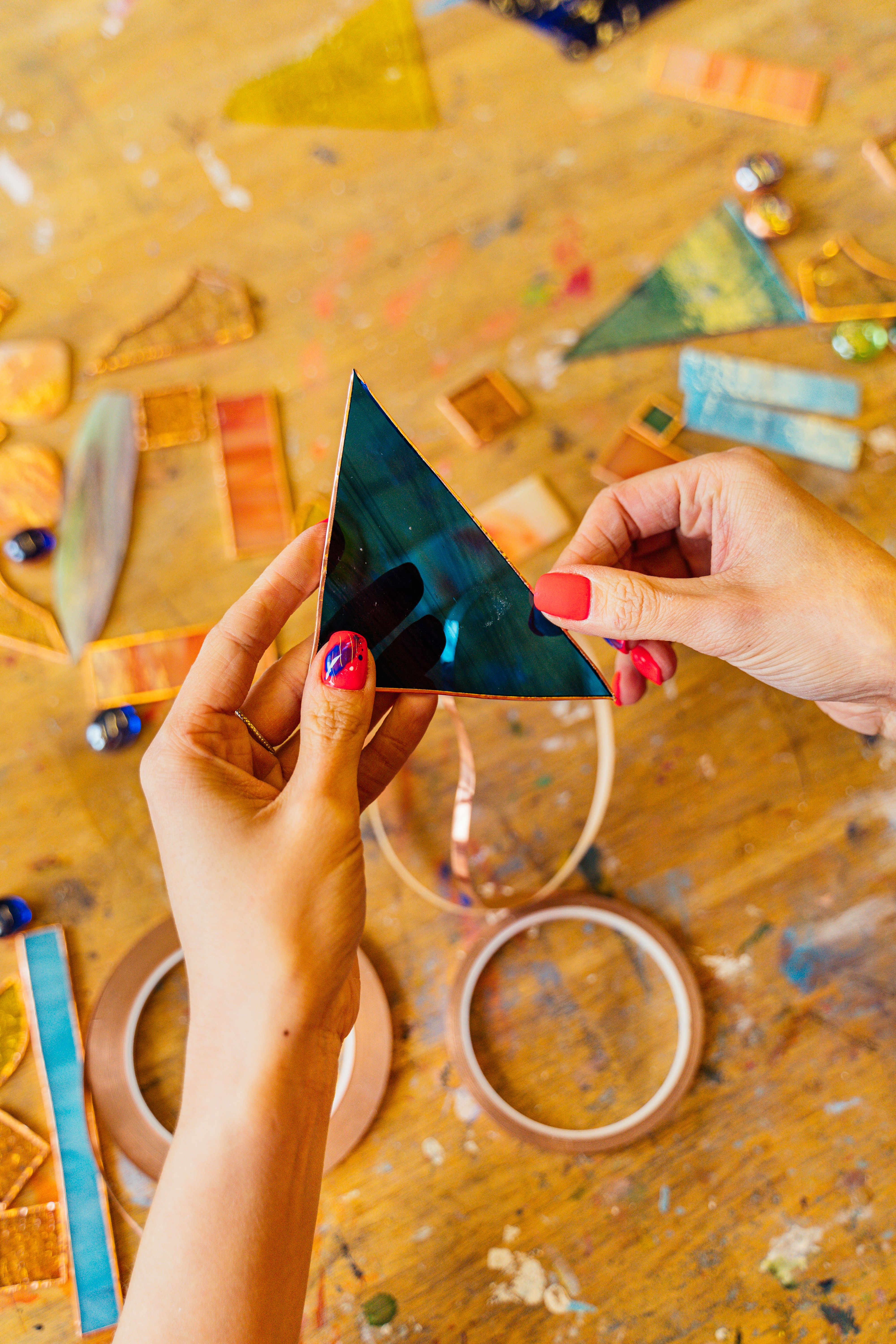 Hands crafting stained glass artwork on a workshop table with colorful glass pieces.
