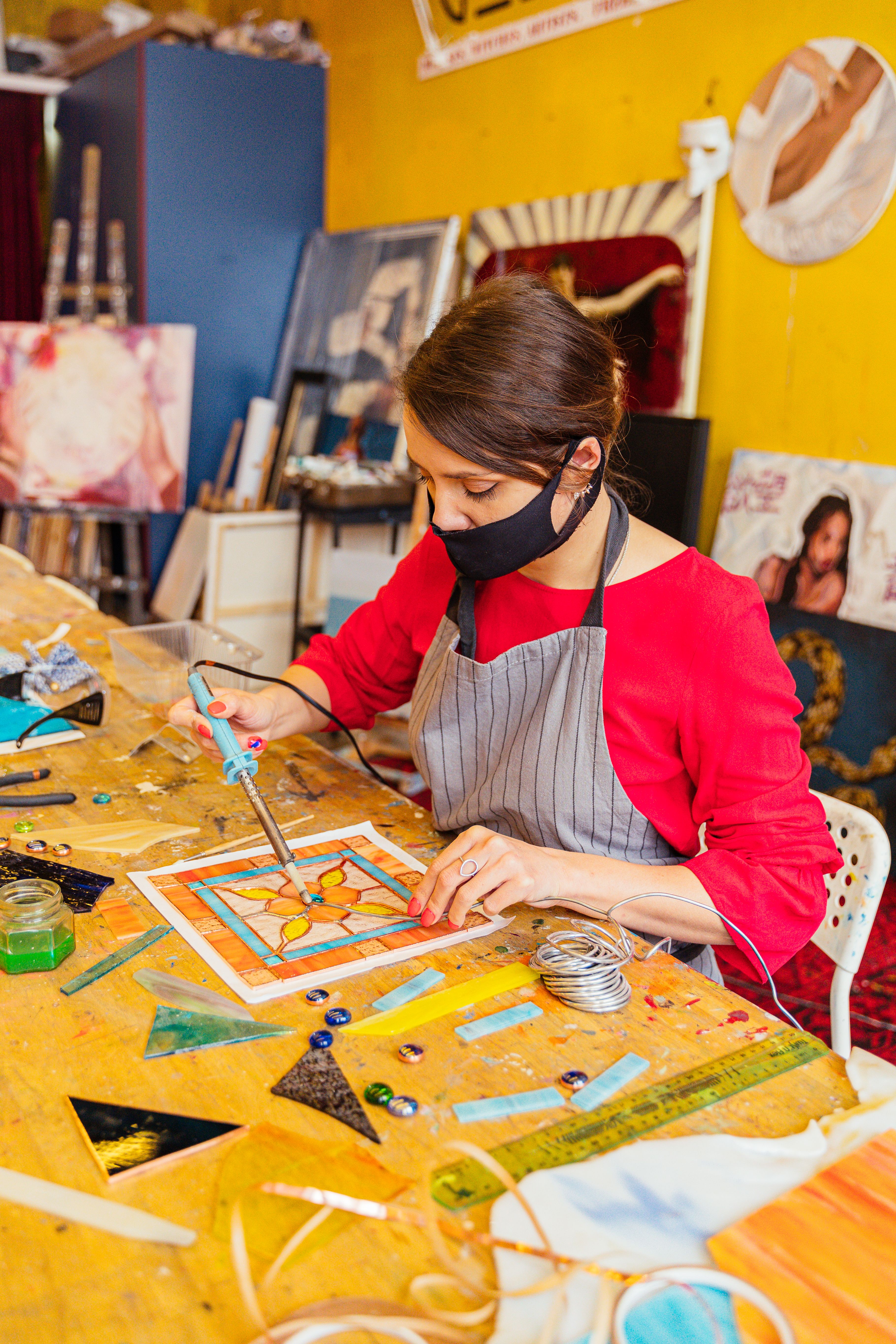 Woman crafting stained glass art in vibrant studio with art supplies and tools.