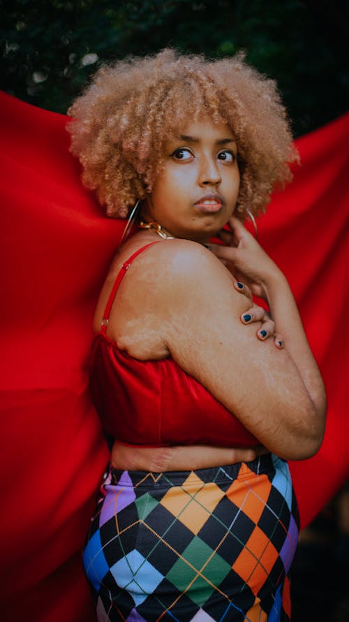 Free Side view of plus size African American female with curly hair showing imperfect skin with stretch marks against red cloth and looking away Stock Photo