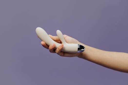 Close-up of a hand holding a dual motor rabbit vibrator against a purple backdrop, emphasizing modern design.