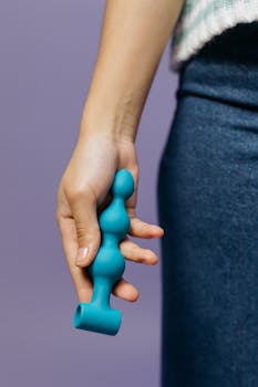 Close-up shot of a hand holding a teal adult toy against a purple background.