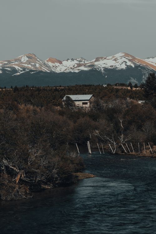Free Idyllic cabin near a river surrounded by snowy mountains and forest in a tranquil setting. Stock Photo