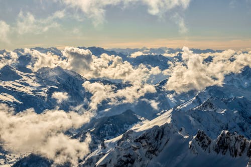 From above picturesque view of high mounts with snow under cloudy sky on sunny day in winter