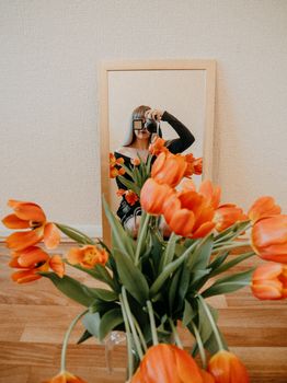 Artistic photo capturing a woman photographing a bouquet of orange tulips with a mirror reflection.