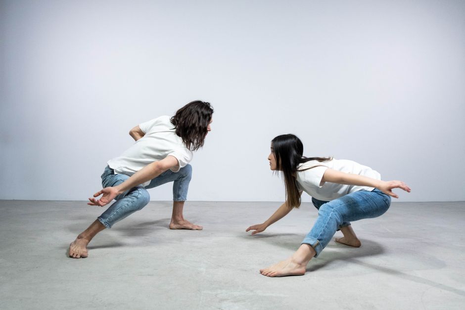 Two adults engaging in dynamic dance poses in a minimalistic studio setting with denim and white attire.