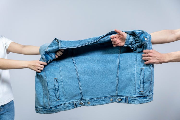 Two People Pulling A Blue Denim Jacket