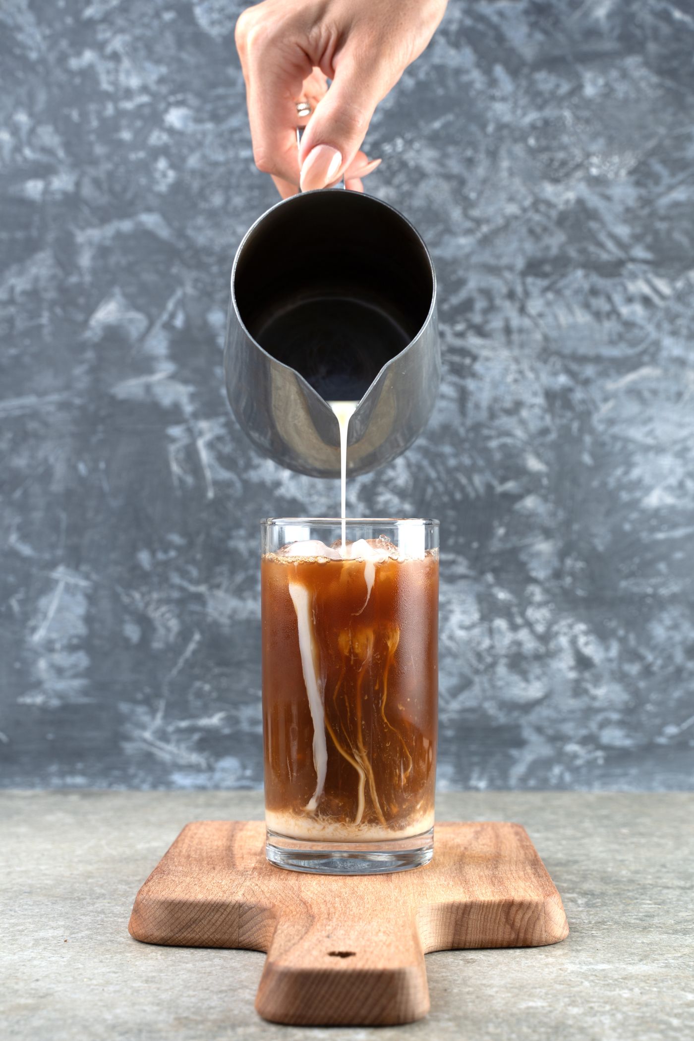 Milk being poured from a pitcher into iced coffee