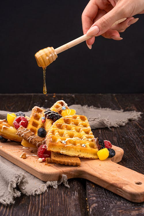 A Person Adding Honey using Dipper to dry fruits and waffles.