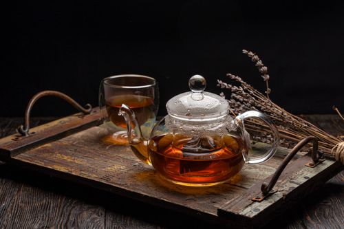 Free A glass teapot with steaming herbal tea on a rustic wooden tray featuring lavender sprigs. Perfect cozy beverage scene. Stock Photo