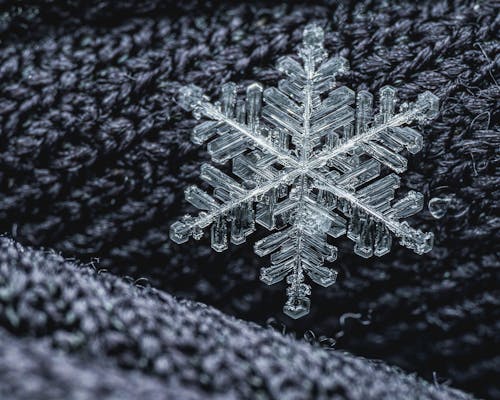 Macro shot of delicate glass snowflake placed on dark woolen surface of warm textile