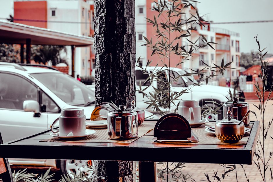 A cozy café setting in Kira Town, Uganda, with outdoor view featuring mugs, sugar bowls, and parked cars.