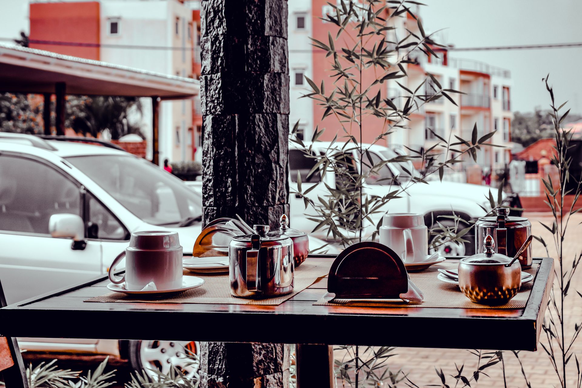 A cozy café setting in Kira Town, Uganda, with outdoor view featuring mugs, sugar bowls, and parked cars.