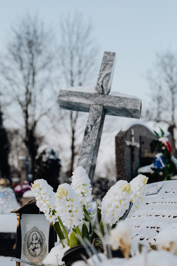 A Concrete Cross Tombstone On A Grave Beside White Flowers