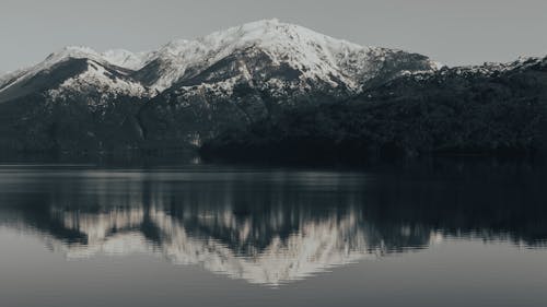 Grayscale Photo of a Snow Covered Mountain Near a Placid Lake