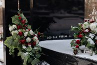 Snow-covered tombstone with red roses and white flowers, symbolizing winter's serene beauty in a cemetery.
