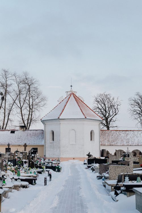 Free A tranquil cemetery in winter featuring a snow-covered chapel and tombstones along a snowy pathway. Stock Photo