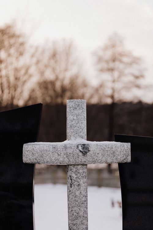 Free A snow-covered stone cross in a tranquil winter cemetery setting, evoking a peaceful atmosphere. Stock Photo