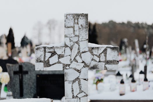 A mosaic cross stands in a snowy cemetery, capturing winter's tranquility and solitude.