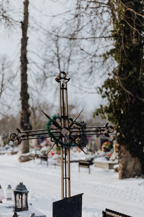 Free A detailed iron cross in a serene snow-covered cemetery, creating a tranquil winter setting. Stock Photo