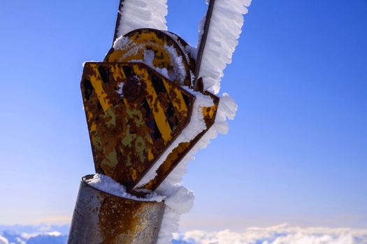 Old metal part with corrosion and striped ornament with snow under blue sky in winter