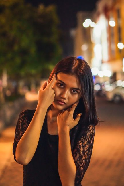 Striking portrait of a woman in black attire posing on an illuminated street at night. Captured in Jawa Barat, Indonesia.