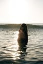 Side view of tranquil young female tourist with long dark hair standing in waving ocean with closed eyes and enjoying summer sunset