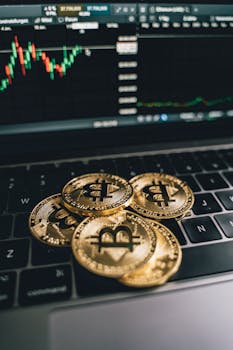 Golden bitcoins on a laptop keyboard with a trading chart in the background, symbolizing digital currency and finance.
