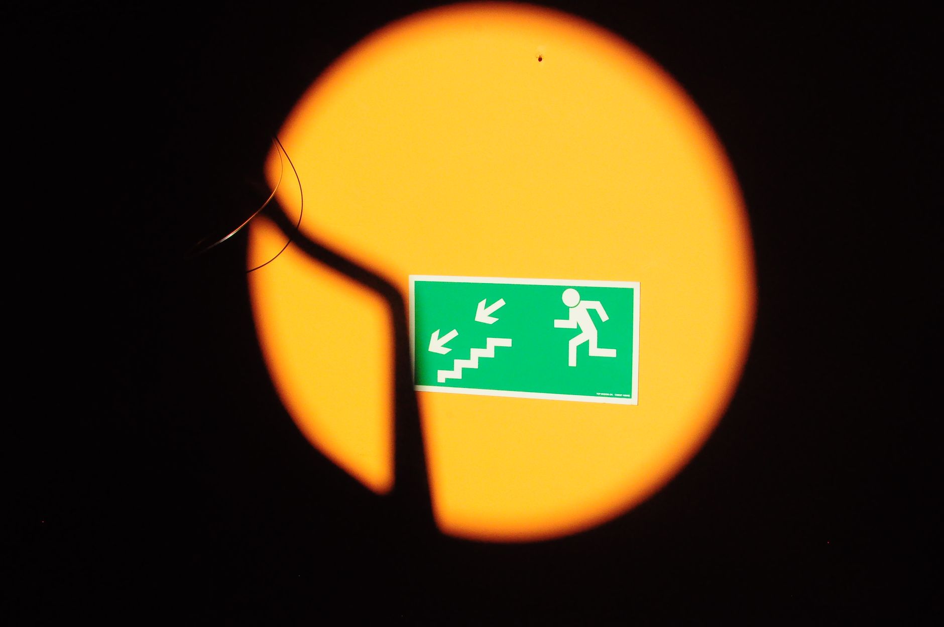 Green emergency exit sign with stairs, highlighted by dramatic lighting and shadows.