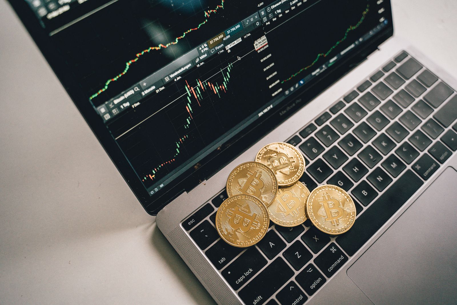 Golden bitcoin coins placed on a laptop keyboard with trading chart displayed on the screen.