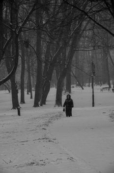 A lone woman walking in a snowy winter park, captured in monochrome.