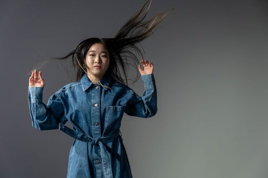 Studio portrait of an Asian woman in denim with wind-swept hair, showcasing fashion and attitude.