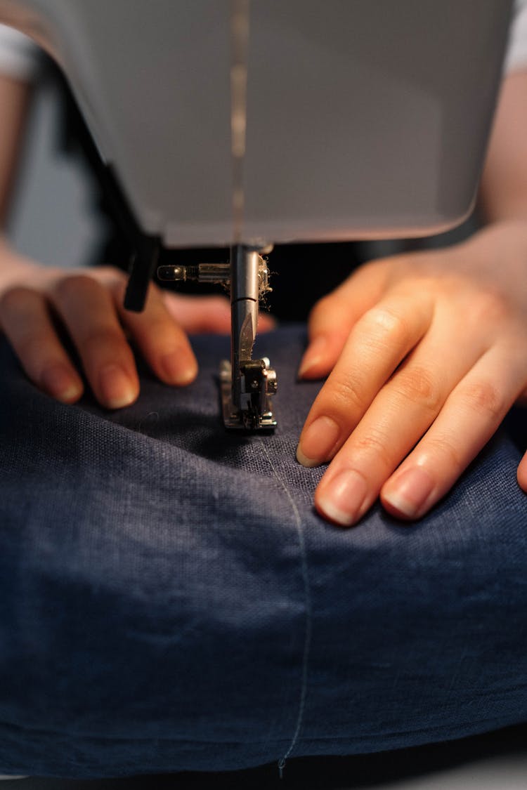 Person's Hand Pushing Fabric In Sewing Machine