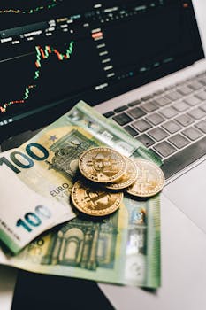 Euro banknotes and Bitcoin coins on a laptop, showcasing finance and cryptocurrency trends.